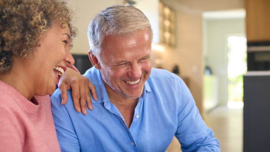 A joyful mature couple at home, laughing and relaxed, symbolizing financial security and peace of mind with SureWealth Solutions' strategies to protect wealth outside the stock market.